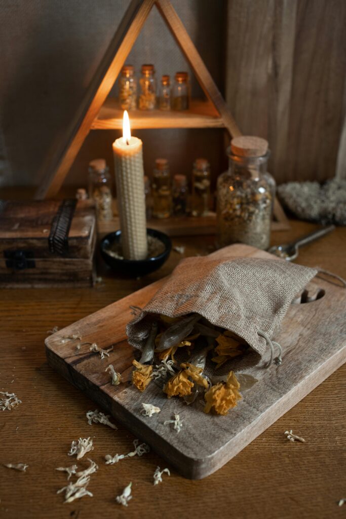 A warm, rustic herbal display with a burning candle and dried flowers on a wooden table.