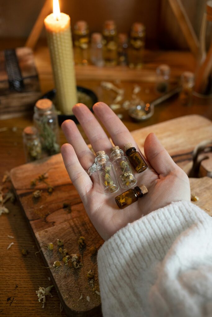 A hand holding small glass vials with dried herbs on a wooden table, candle-lit ambiance.