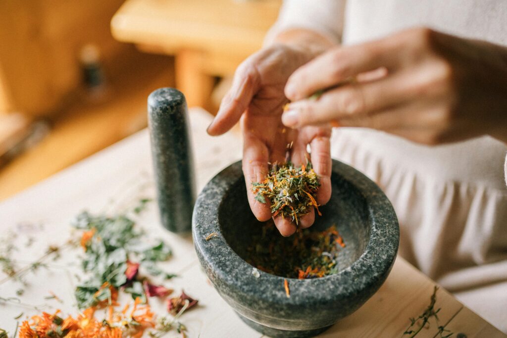 A woman uses a mortar and pestle to crush dried herbs for traditional medicine preparation.