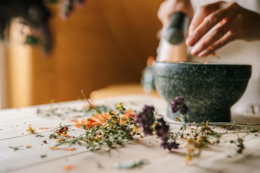 Close-up of hands using mortar and pestle to grind dried flowers on wooden table.