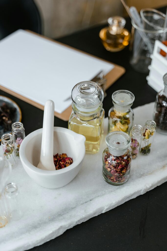 Elevated view of an aromatherapy setup featuring a mortar and pestle, glass bottles, and dried petals on a marble surface.