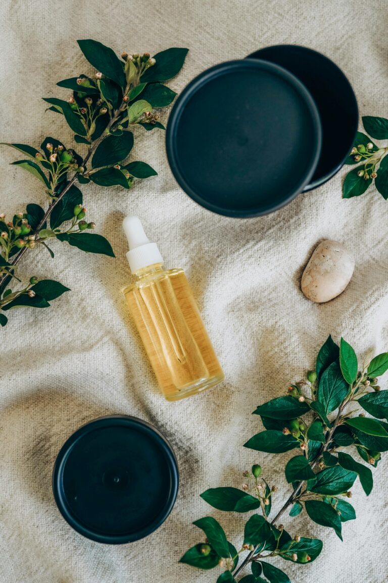 Glass bottle of yellow serum surrounded by green leaves on fabric, showcasing botanical skincare.